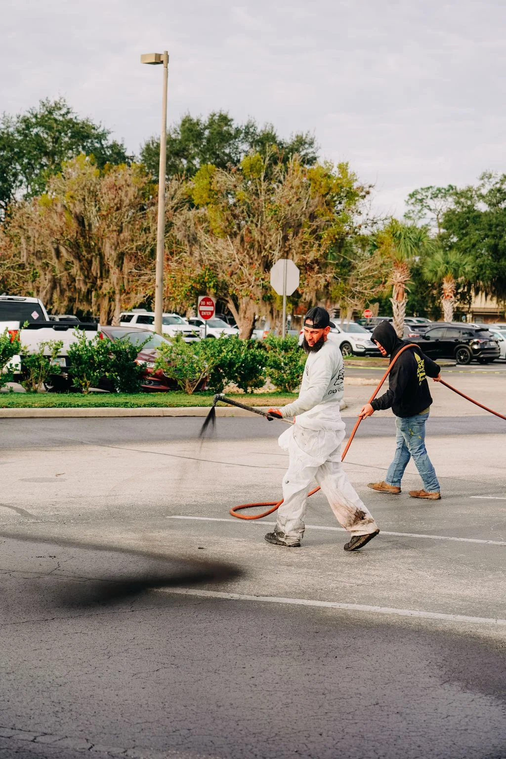 Technicians applying sealcoat to parking lot asphalt with spray equipment and squeegee