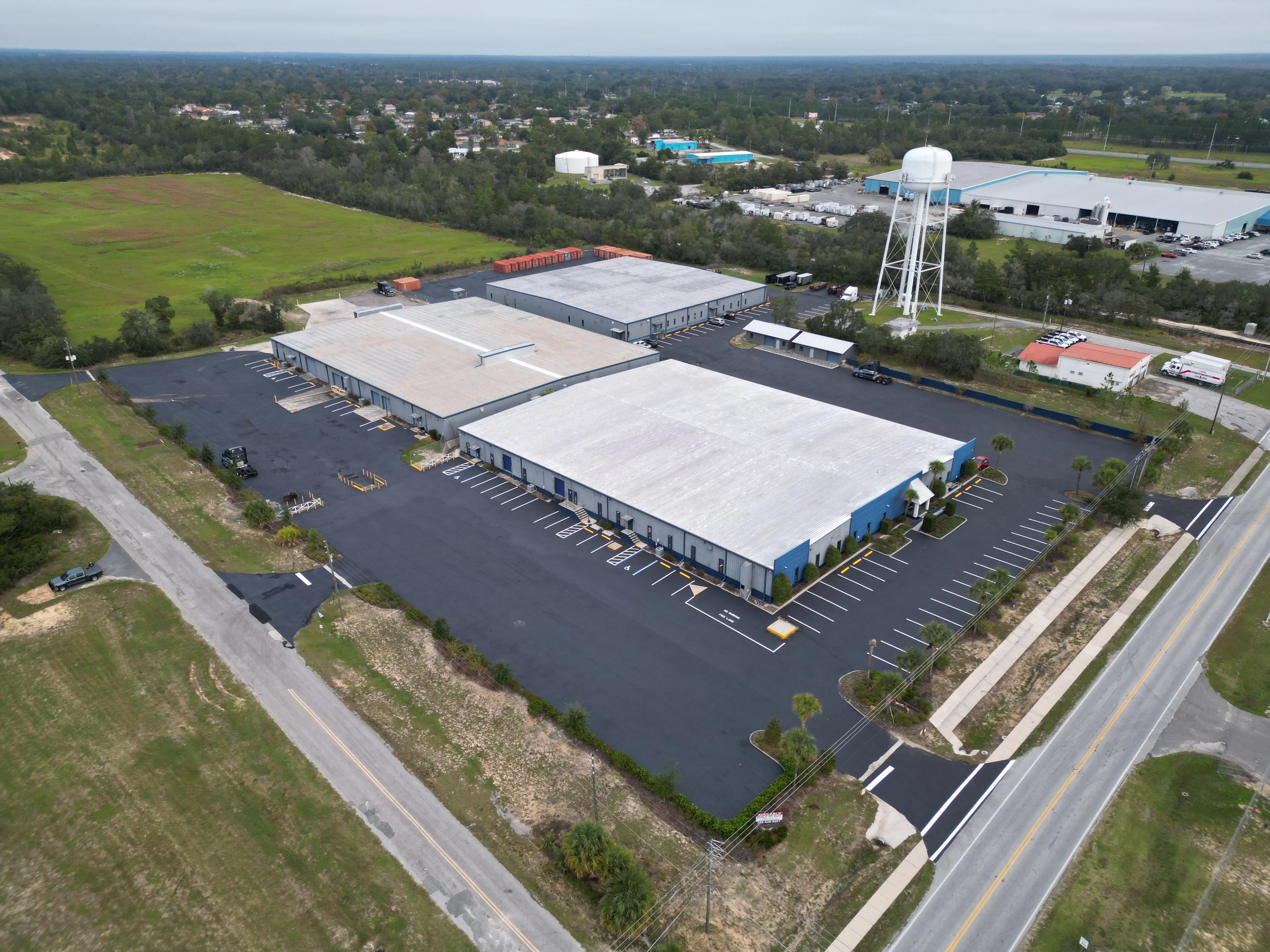 Aerial view of newly paved and sealed commercial parking lot with warehouse buildings and landscaping