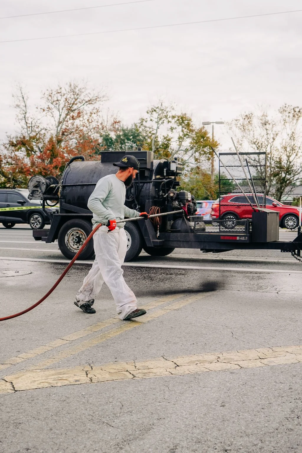 Technician applying sealcoat to parking lot with spray equipment and truck