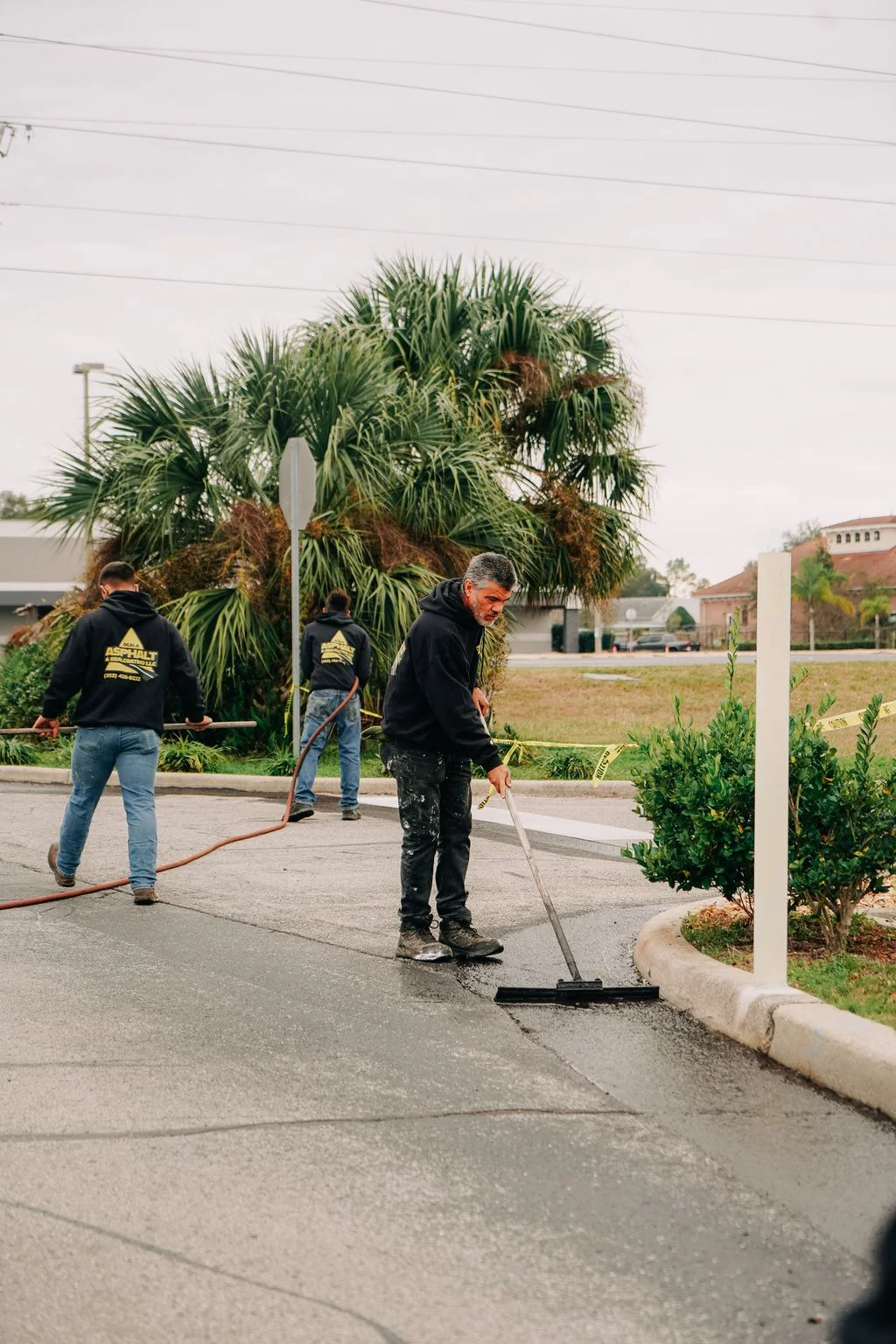Crew applying sealcoat to commercial parking lot with squeegee and hose equipment