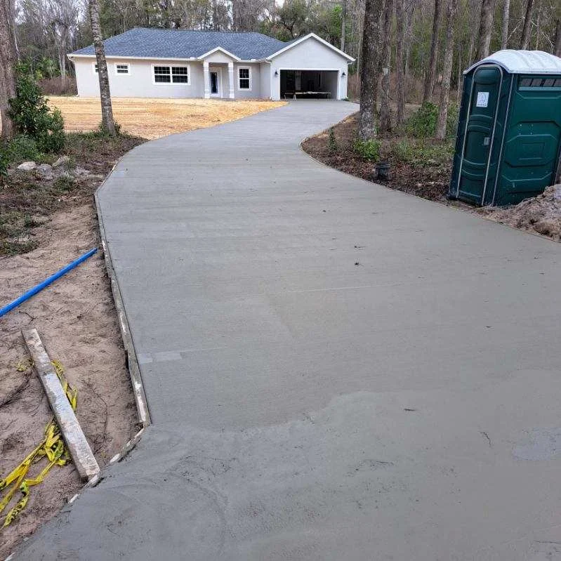 Newly poured concrete driveway curving toward white residential home with garage