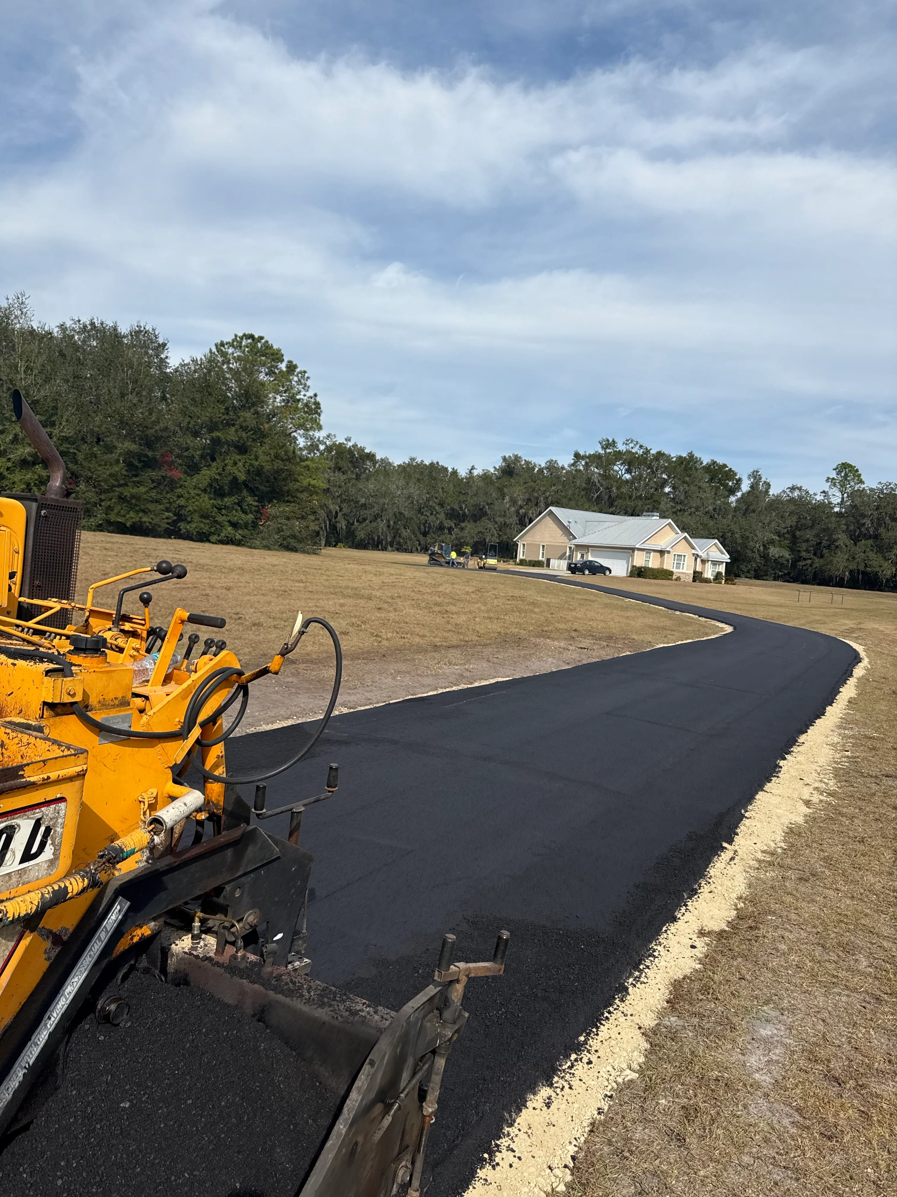 Yellow asphalt paver laying fresh black asphalt on curved residential driveway in Ocala