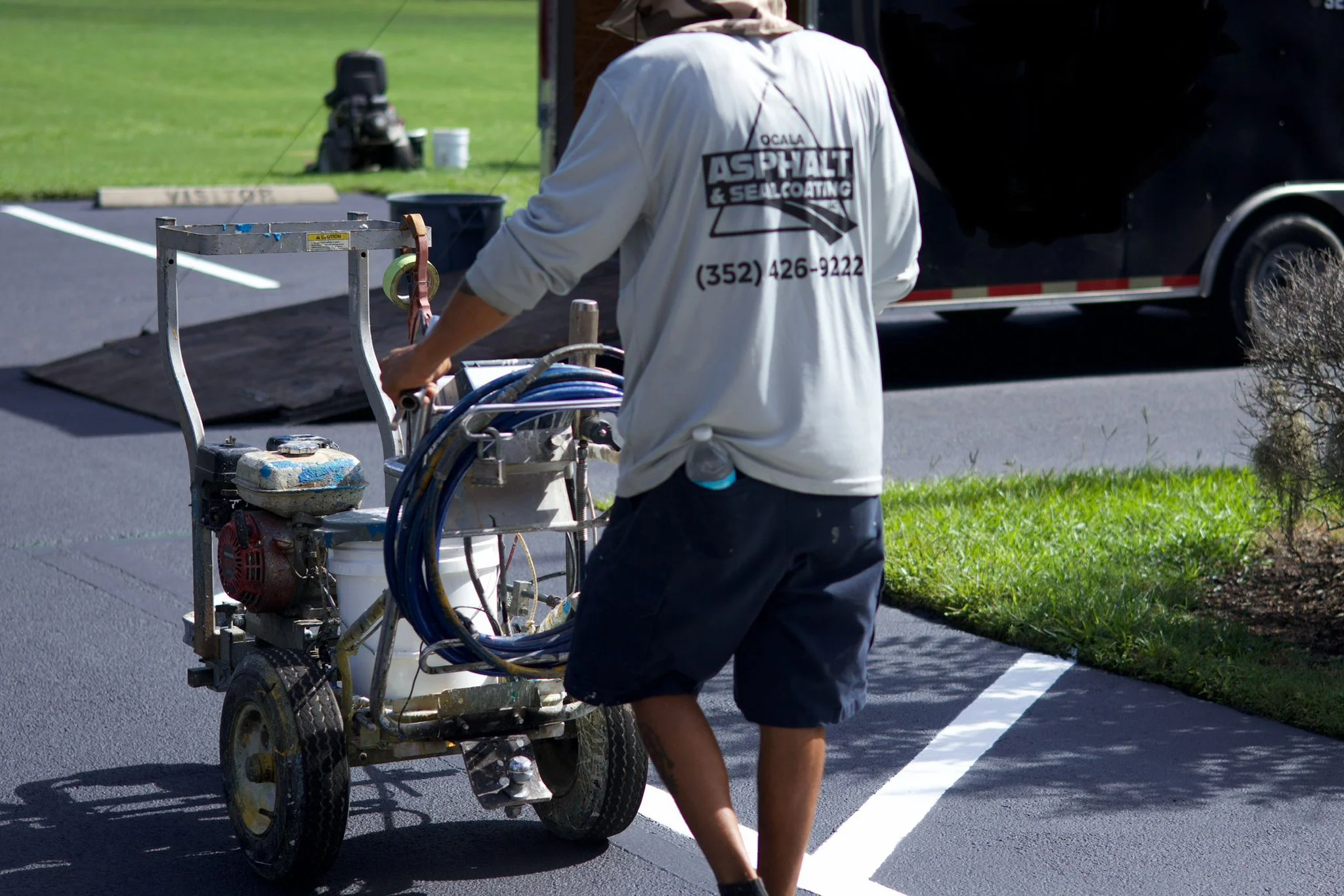 Technician applying sealcoat to asphalt driveway with spray equipment