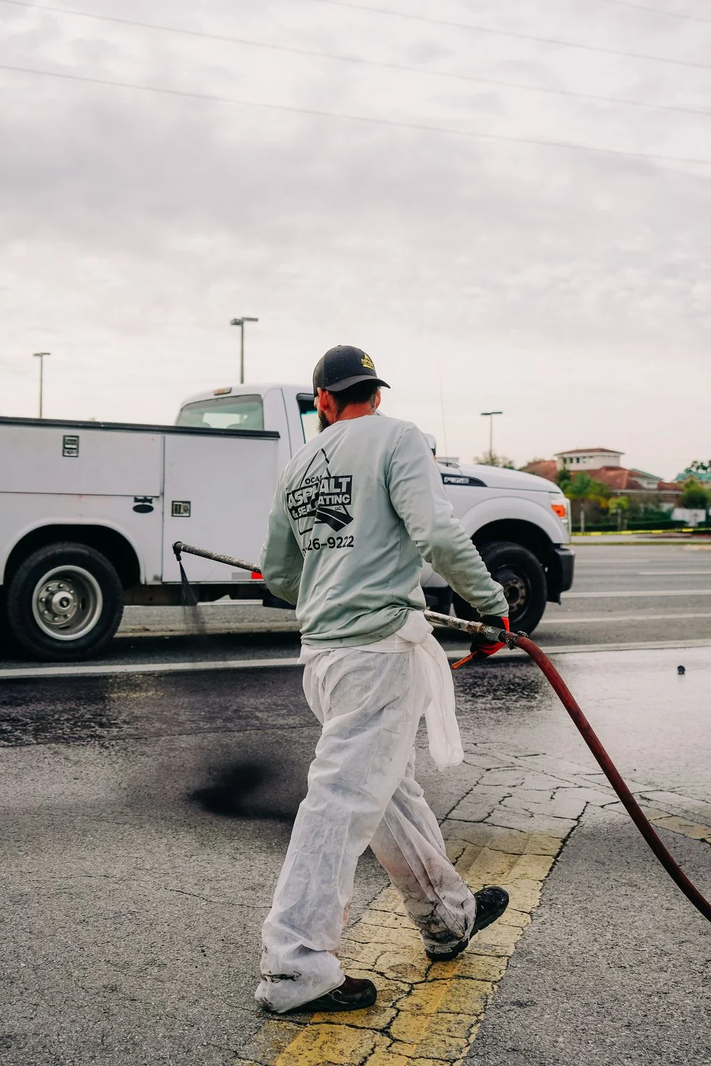 Technician applying sealcoat to parking lot asphalt with service truck in background