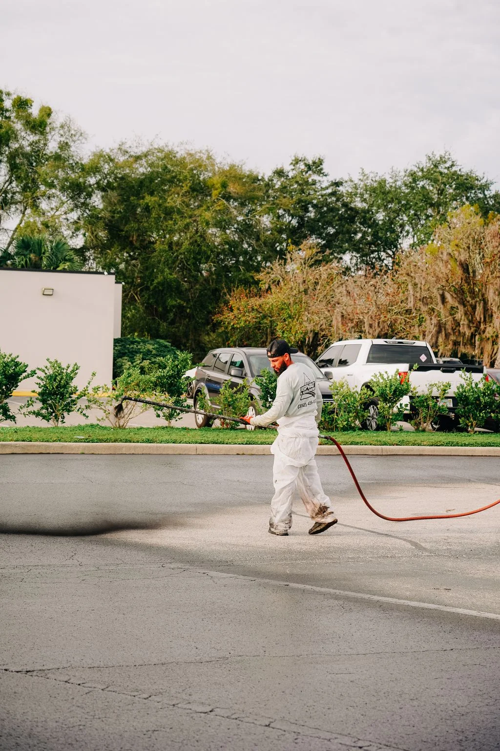 Technician applying sealcoat to asphalt driveway with spray hose equipment