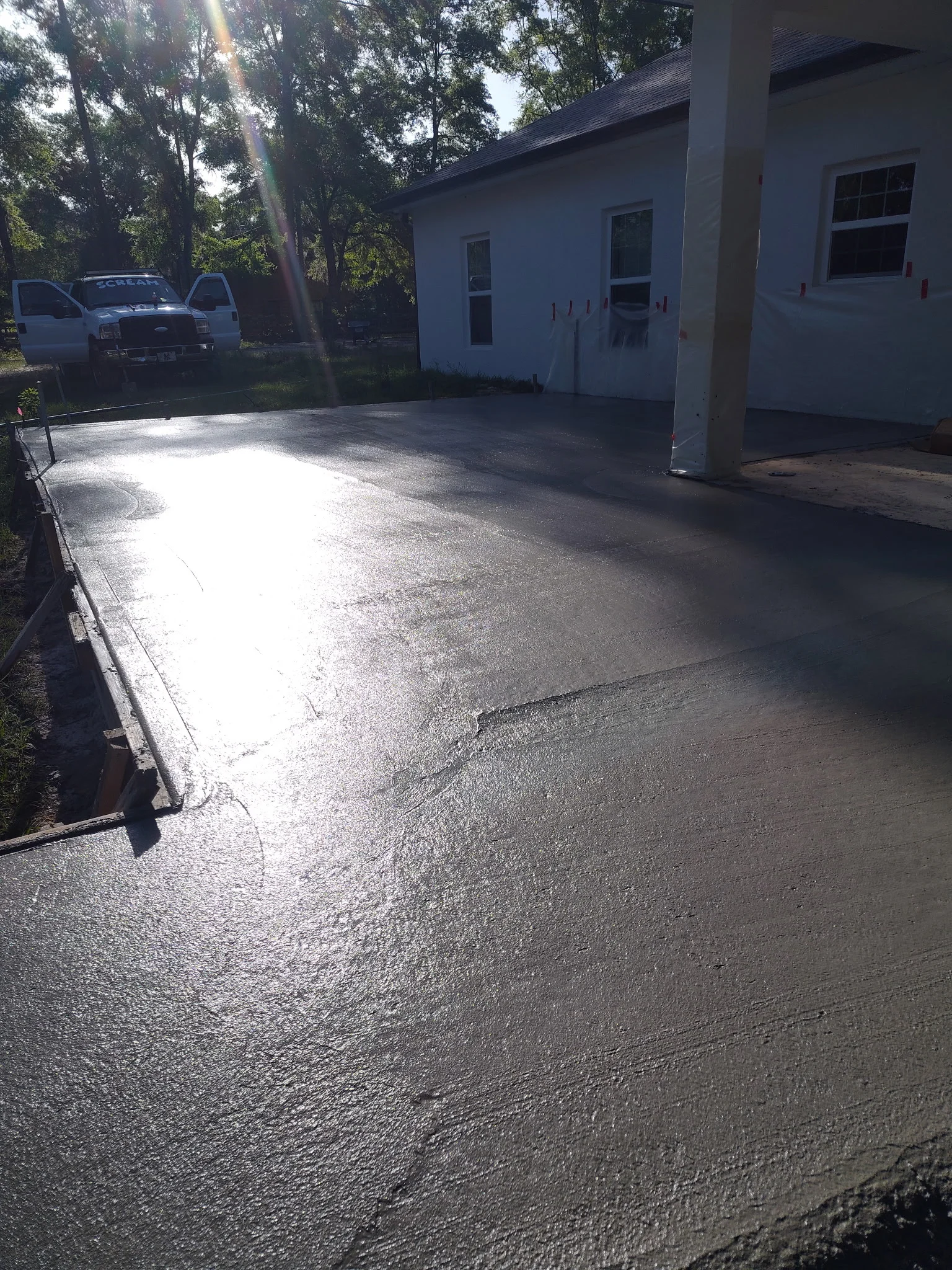 Newly paved black asphalt driveway with white house and trees in background