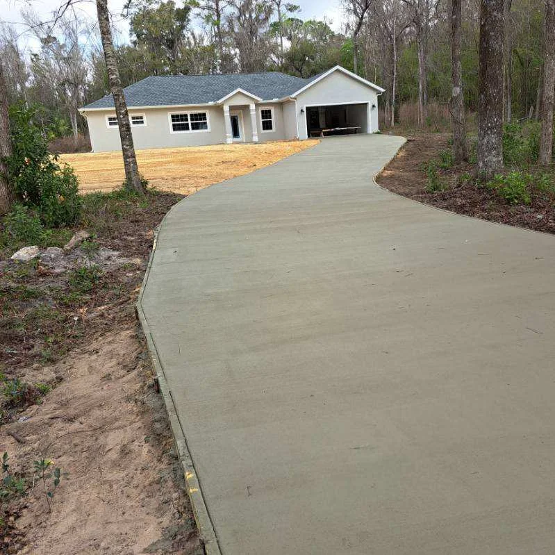Newly installed curved concrete driveway leading to white home with two-car garage
