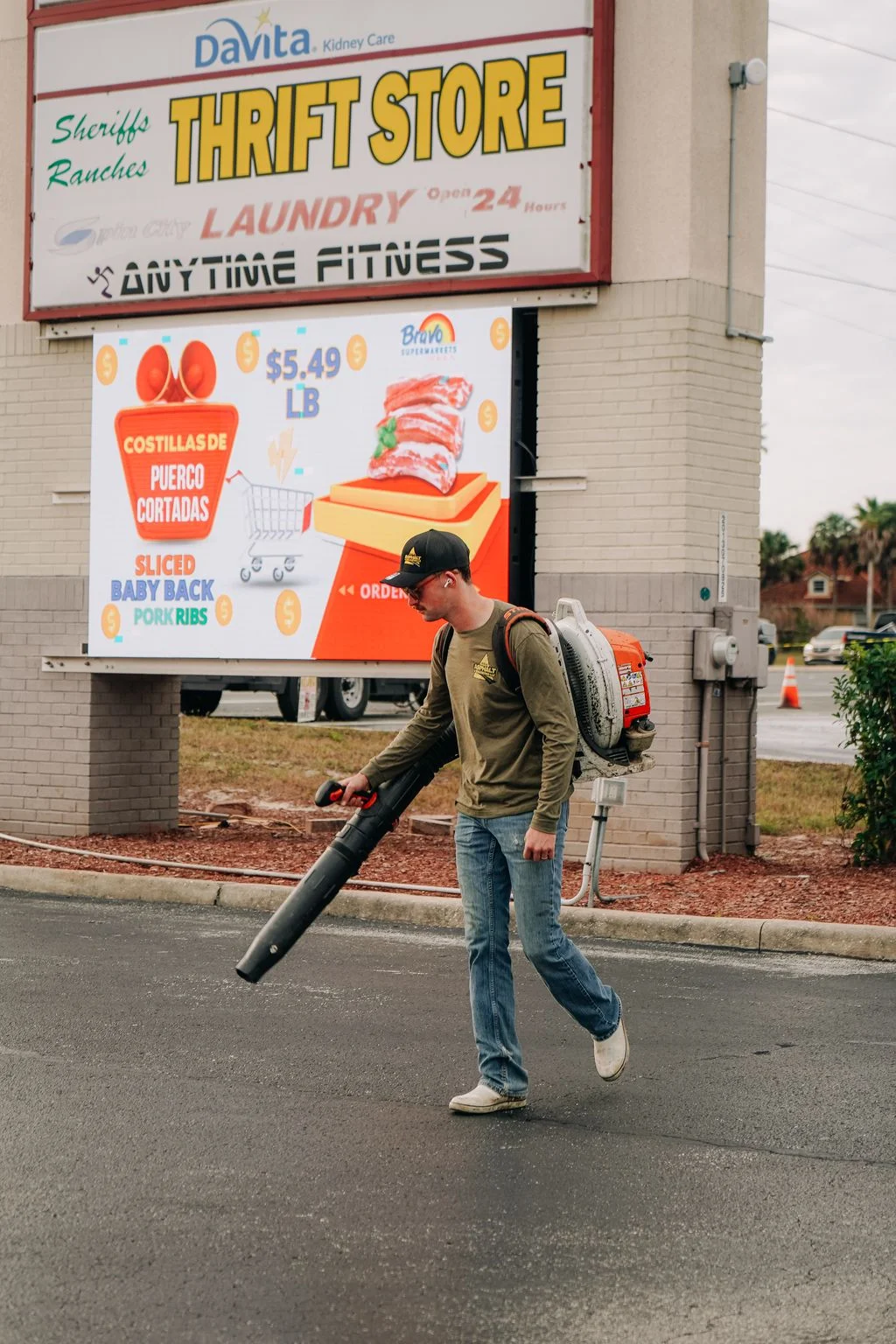Worker using leaf blower to clean commercial parking lot at retail center in Ocala