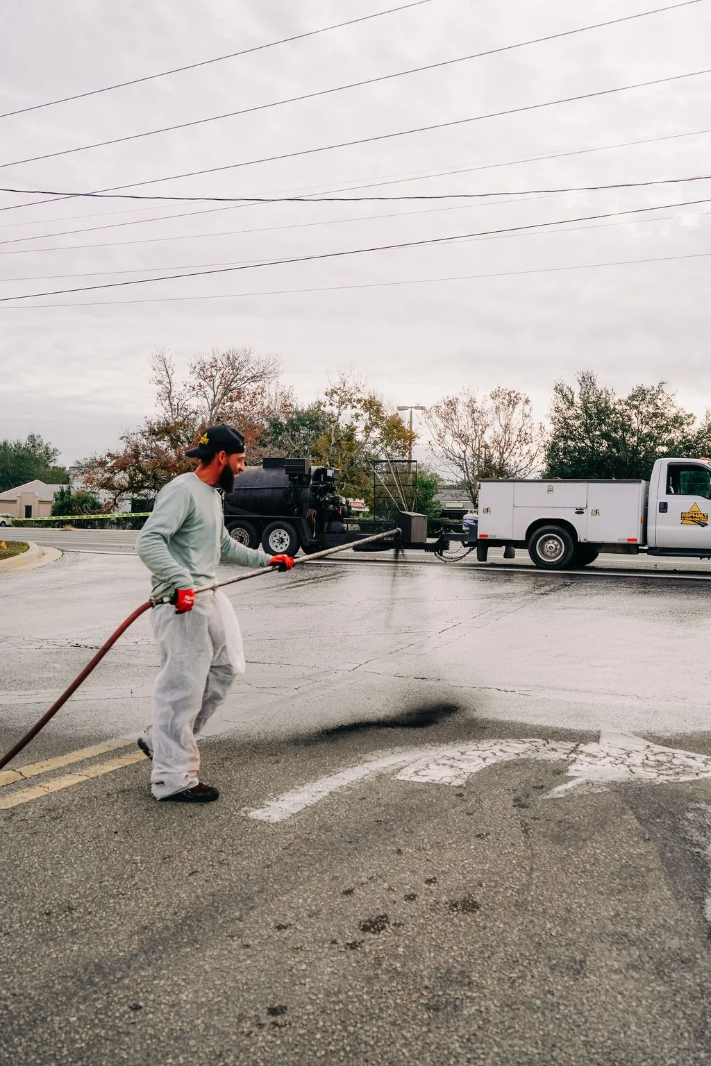 Worker applying sealcoat to parking lot with spray equipment and service truck