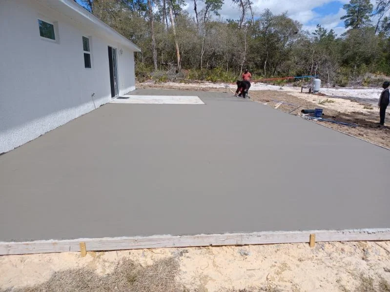 Newly poured concrete driveway with smooth finish next to white house and pine trees