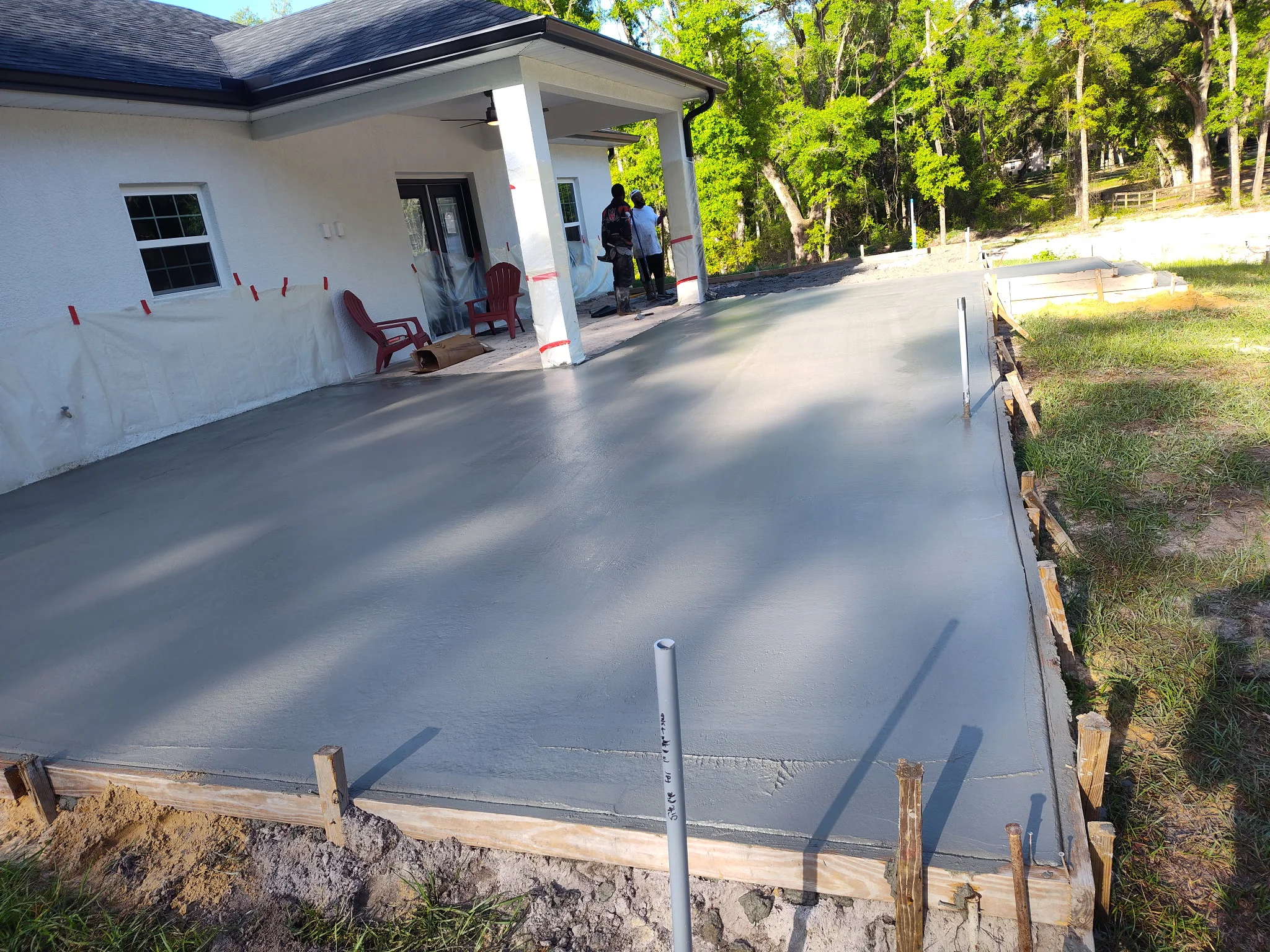 Newly poured concrete driveway with smooth finish next to white residential home